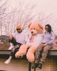two people sitting on top of a roof with a teddy bear