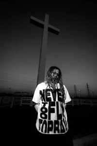a black and white photo of a man standing in front of a cross